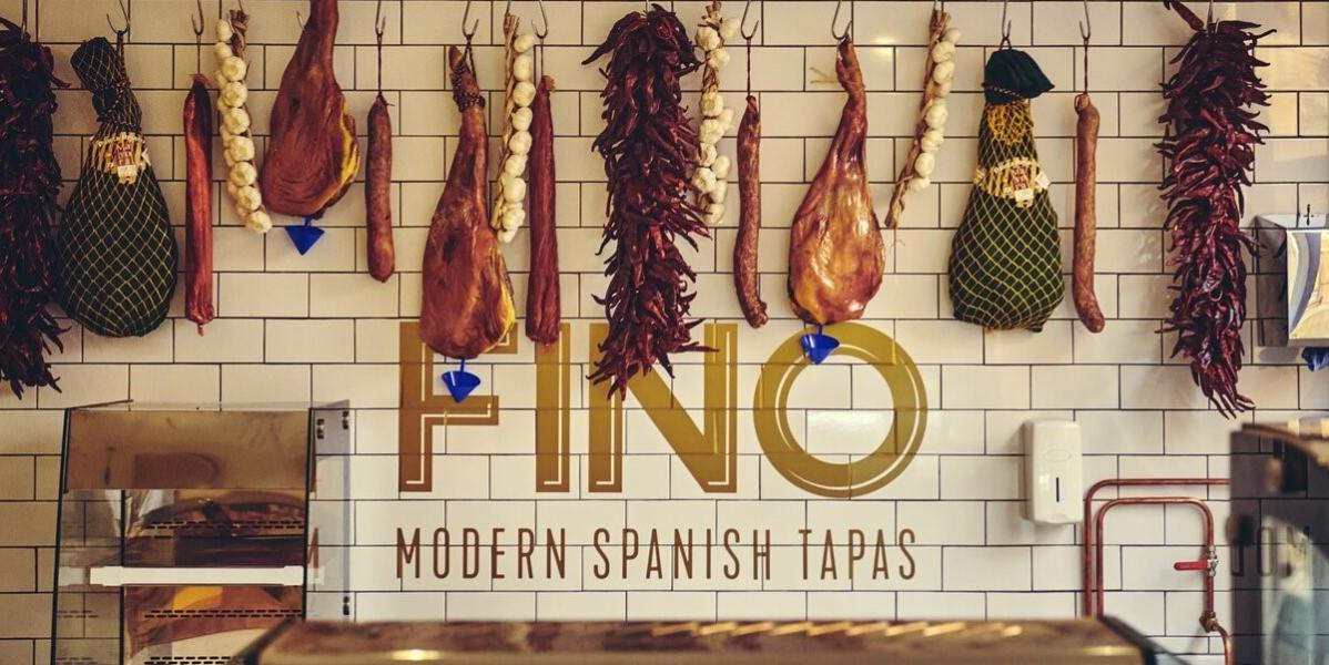 Fino Tapas deli counter A variety of meats hung on a wall above a sign saying "Fino Modern Spanish Tapas"