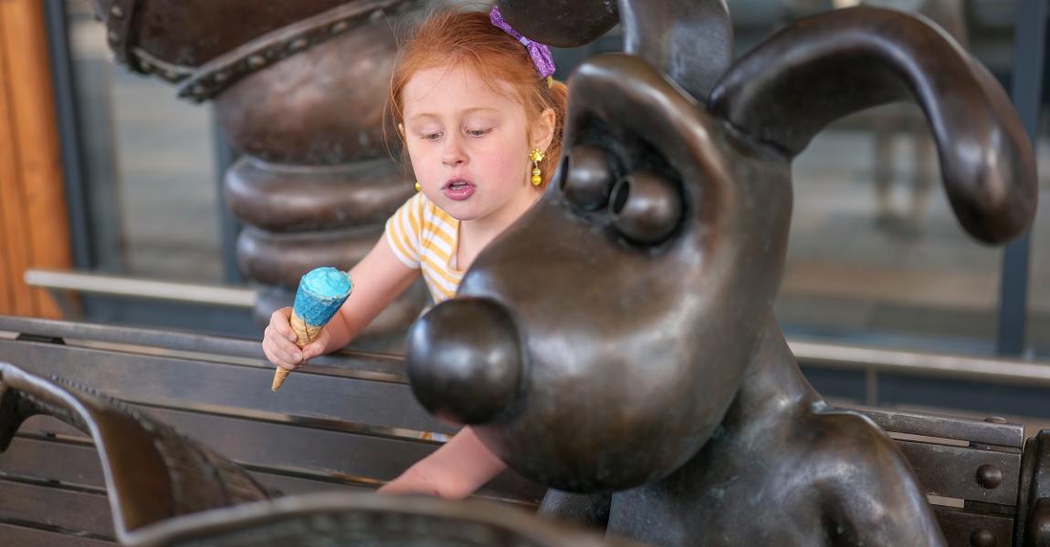Girl with ice cream interacting with Wallace and Gromit statue