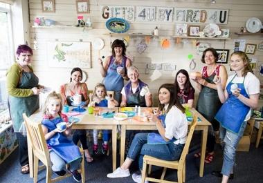 Adults and children painting pottery around a table