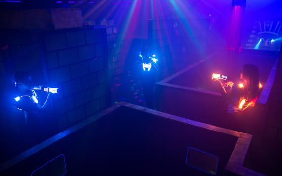 Boy aiming his laser tag gun at camera from behind bars in Laser Quest arena.