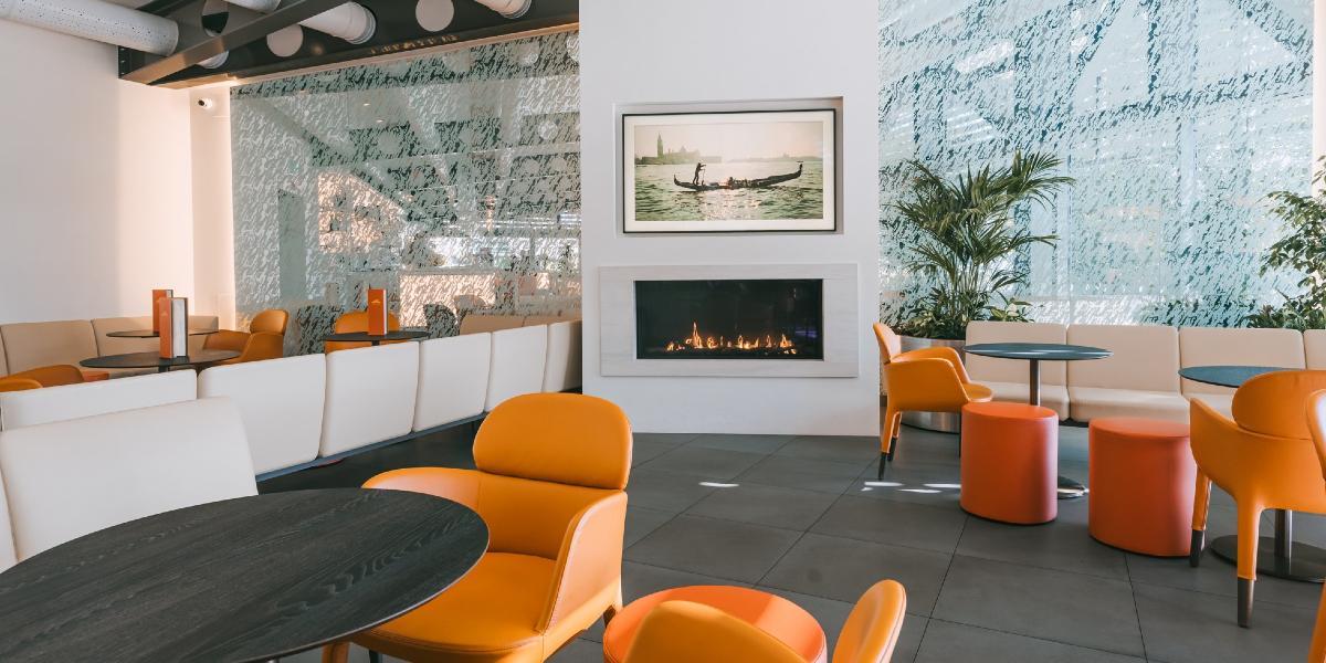 Main image: Orange seating and modern fire inside Italian Orchard's dining area. Orange seating and modern fire inside Italian Orchard's dining area.