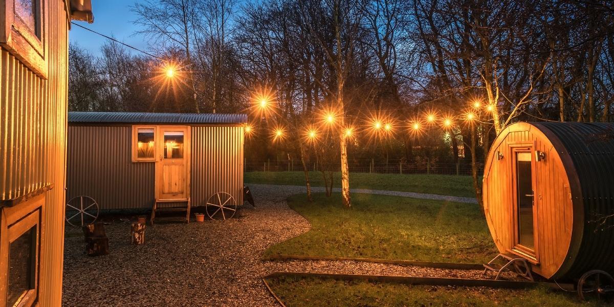 Main image: Samlesbury Hall's shepherd huts lit up at night with string lights. Samlesbury Hall's shepherd huts lit up at night with string lights.