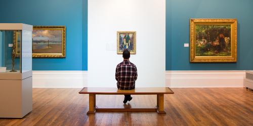 Page icon: Man sat looking at painting. Man sat on bench admiring painting on wall inside Harris Gallery, Preston.