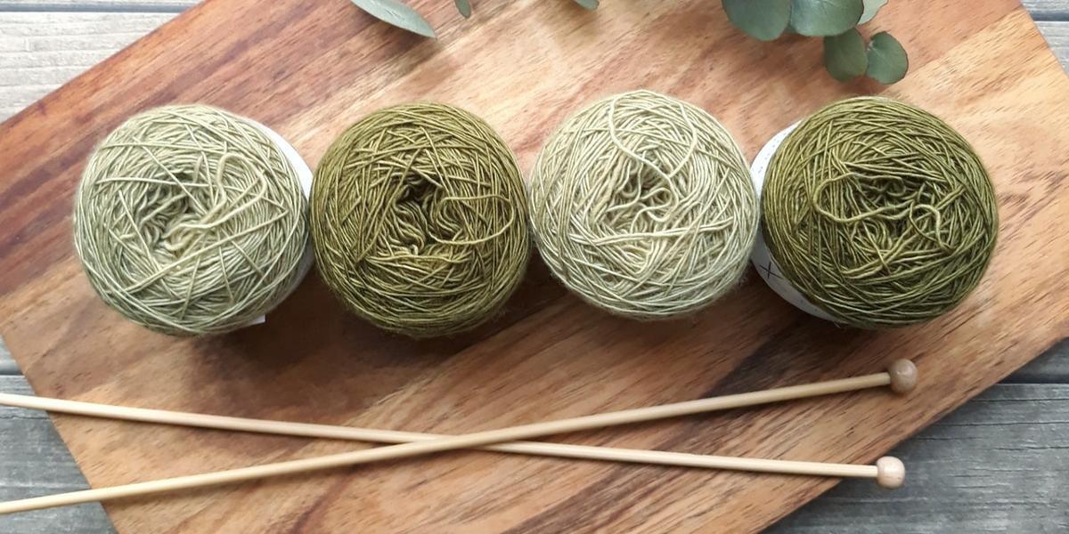 Main image The Knit Wits Craft Group Different shades of balls of wool arranged in row on wooden board with knitting needles beside them.