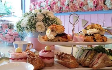 Afternoon tea at Mad Hatters arranged on a table around some flowers.