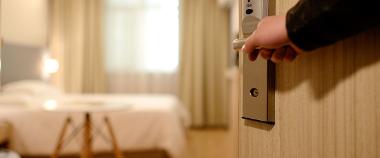 Person opening door to hotel room, with bed visible inside.