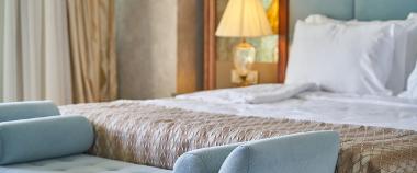 Hotel room bed with lamp on bedside and seating at its foot.