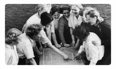 Dick Kerr Ladies football team huddled around strategy plan on table.